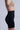 Against a plain background, a person in beige bra and TITSY TUMMY TUCK SHORTS IN BLACK is shown from the side, highlighting the sleek fit, seamless hems, and contouring of the high-rise shapewear.