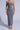 A person dons form-fitting, ankle-length gray Titsy Tummy Tuck shorts with seamless hems. Strappy white heels complete the chic outfit against a plain light-gray background.