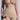 A person in high-waisted TAN TITSY TUMMY TUCK shorts and a nude bra is shown from the neck down. An inset reveals the same individual before wearing the shorts, in a black bra with noticeable midriff differences highlighted by their high-rise fit.
