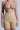 An individual showcases the TITSY TUMMY TUCK SHORTS IN TAN against a plain backdrop. The seamless hems highlight a smooth fit, and the high-rise design enhances the upper body, emphasizing the texture and graceful contour of each garment.