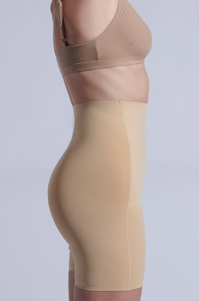 A person models the TITSY TUMMY TUCK SHORTS IN TAN, highlighting the seamless hems and high-rise fit from a side view against a plain background. 8
