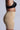 A person in profile showcases sleek TITSY TUMMY TUCK SHORTS IN TAN. These high-rise fit shapewear shorts have seamless hems that smooth the silhouette, set against a simple light gray background that highlights their elegance.