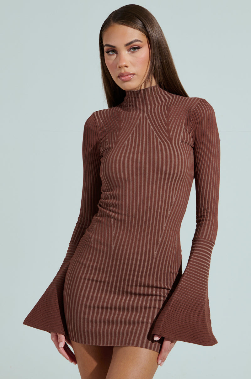 A woman stands against a plain light background wearing the ALL CAUGHT UP KNIT MINI DRESS, a fitted brown ribbed mini dress with elegant bell sleeves flaring at the cuffs.