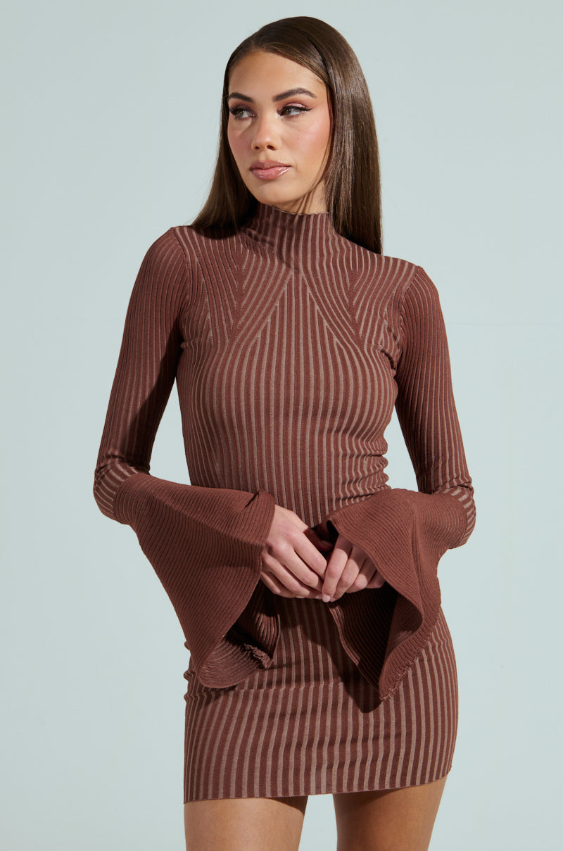 A person with long brown hair wears the ALL CAUGHT UP KNIT MINI DRESS, featuring a fitted, brown striped design and bell sleeves. They stand against a light green background, looking to the side.