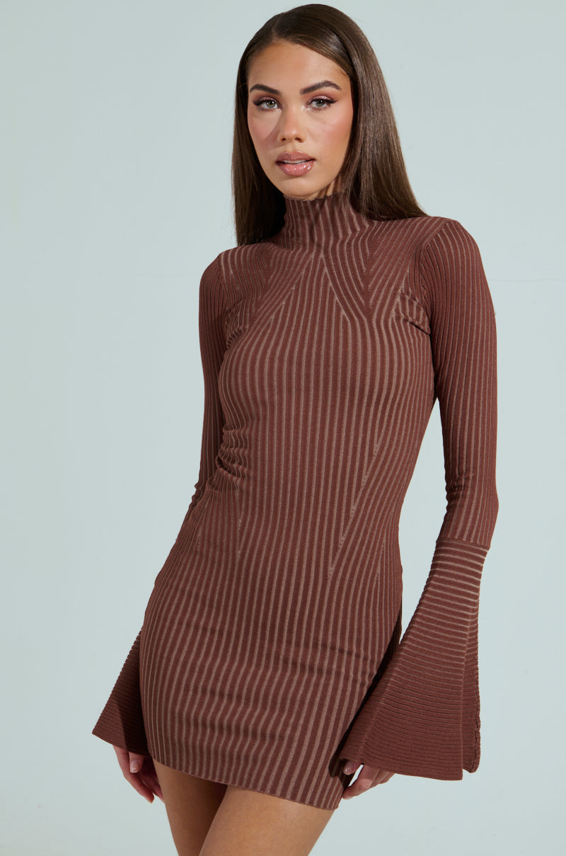 A woman elegantly poses against a plain background in the ALL CAUGHT UP KNIT MINI DRESS, a brown ribbed knit with a high neck and bell sleeves, featuring vertical stripes. Her long hair flows gracefully in the scene.