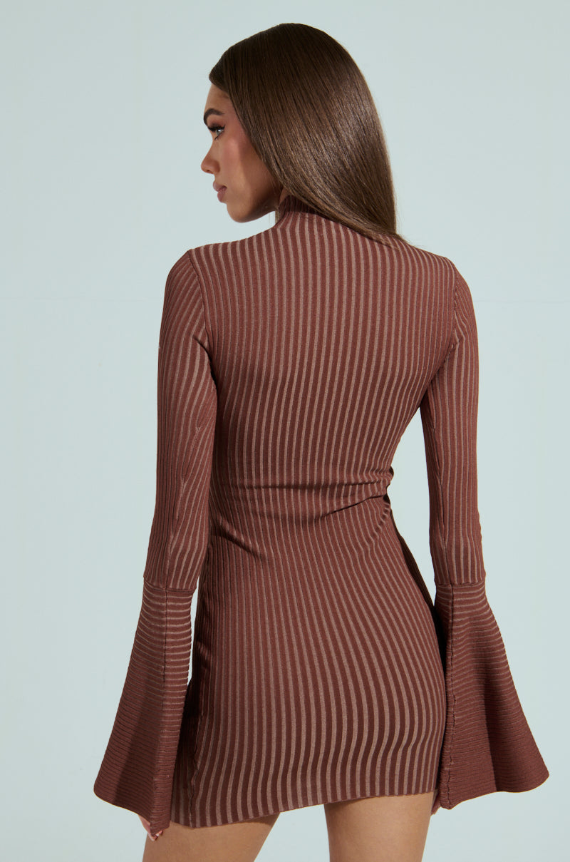 A woman with long hair faces away in the ALL CAUGHT UP KNIT MINI DRESS, a brown striped mini dress with bell sleeves. The backdrop is a soft light teal.