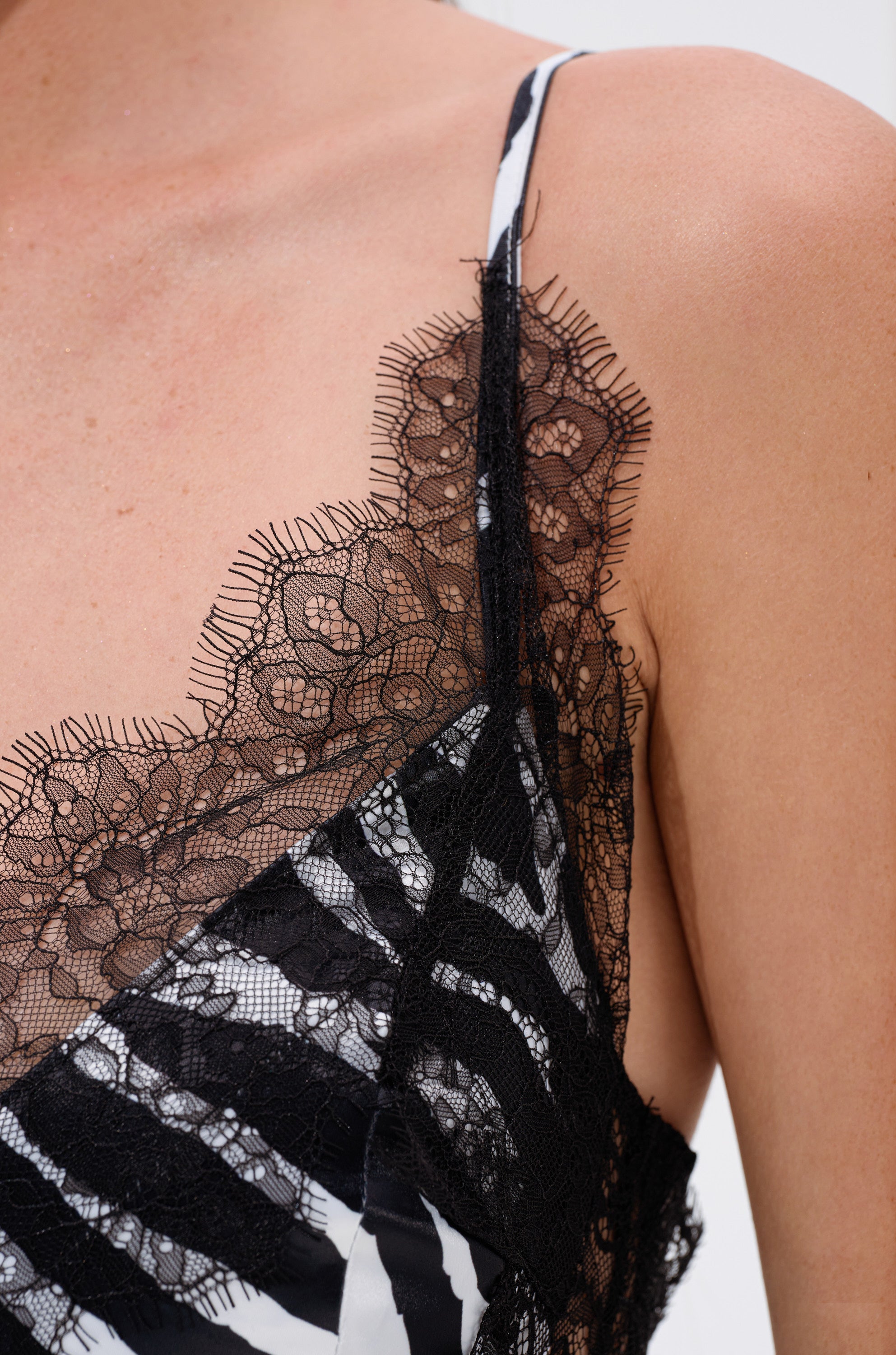 Close-up of a person wearing the SHOW US WHAT YOU GOT SATIN MINI DRESS IN ZEBRA PRINT, featuring bold black and white stripes, delicate see-through floral lace trim along the neckline, and thin shoulder straps for an elegant look.