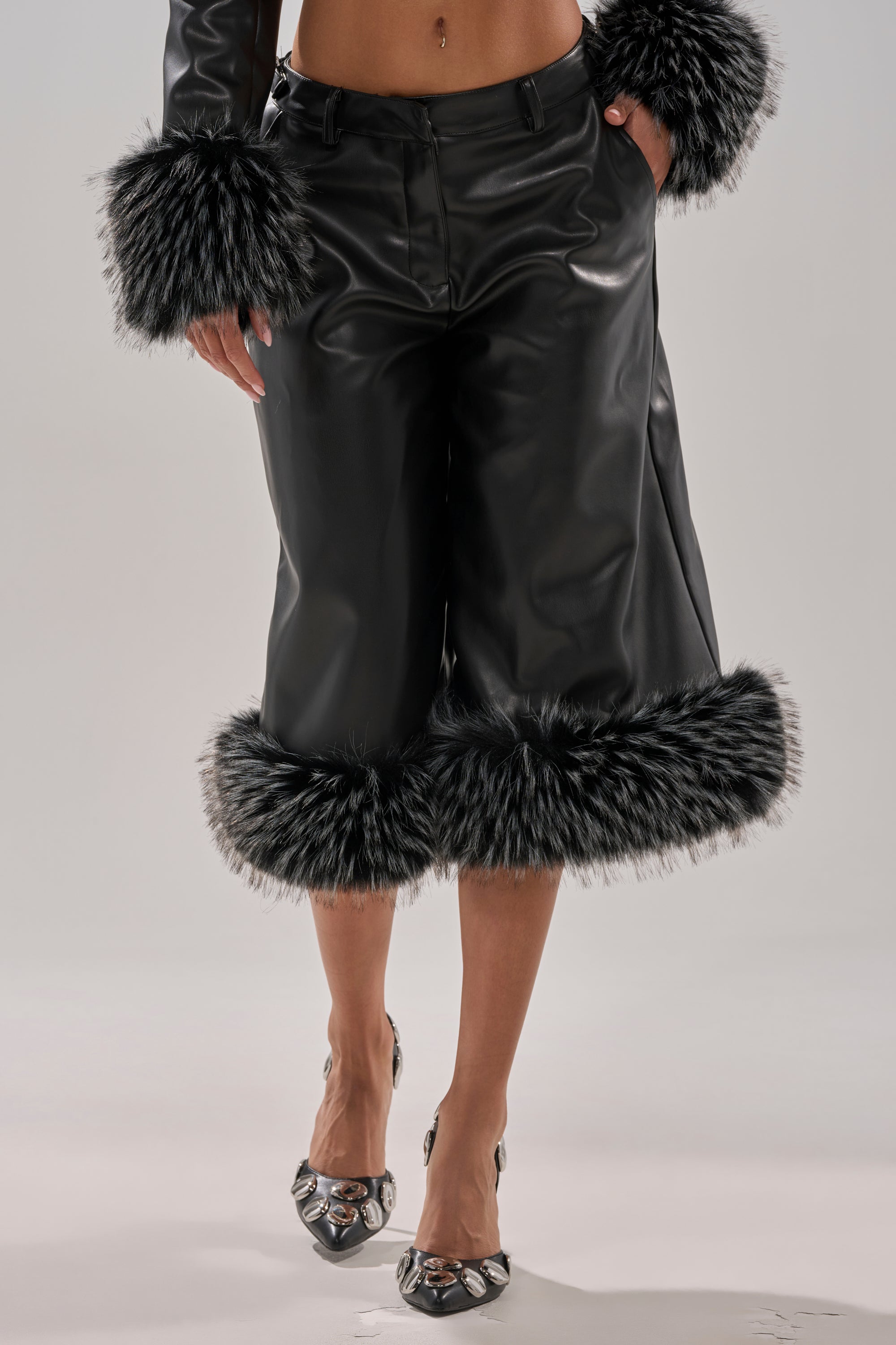 Wearing MIND YOUR OWN FUR TRIM BERMUDA SHORTS with matching black faux leather jacket, both featuring bold black-and-white faux fur trim. Silver metallic-detailed heels complete the visible lower body look.