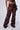 A person wearing the DESERT VIBE CARGO PANT IN BURGUNDY, featuring a high rise with multiple pockets and silver rivet details, paired with black shoes. The image is cropped to show only the person's torso and legs, standing against a plain background.