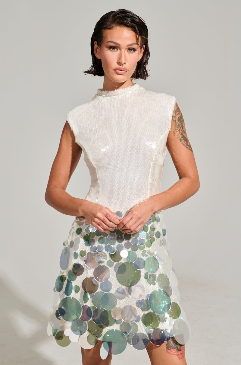 A person with short dark hair is confidently standing against a plain backdrop, wearing the ALL THE RIGHT WAYS SEQUIN MINI DRESS. Adorned with large, reflective sequins, they exude charm and elegance in this party-ready ensemble.