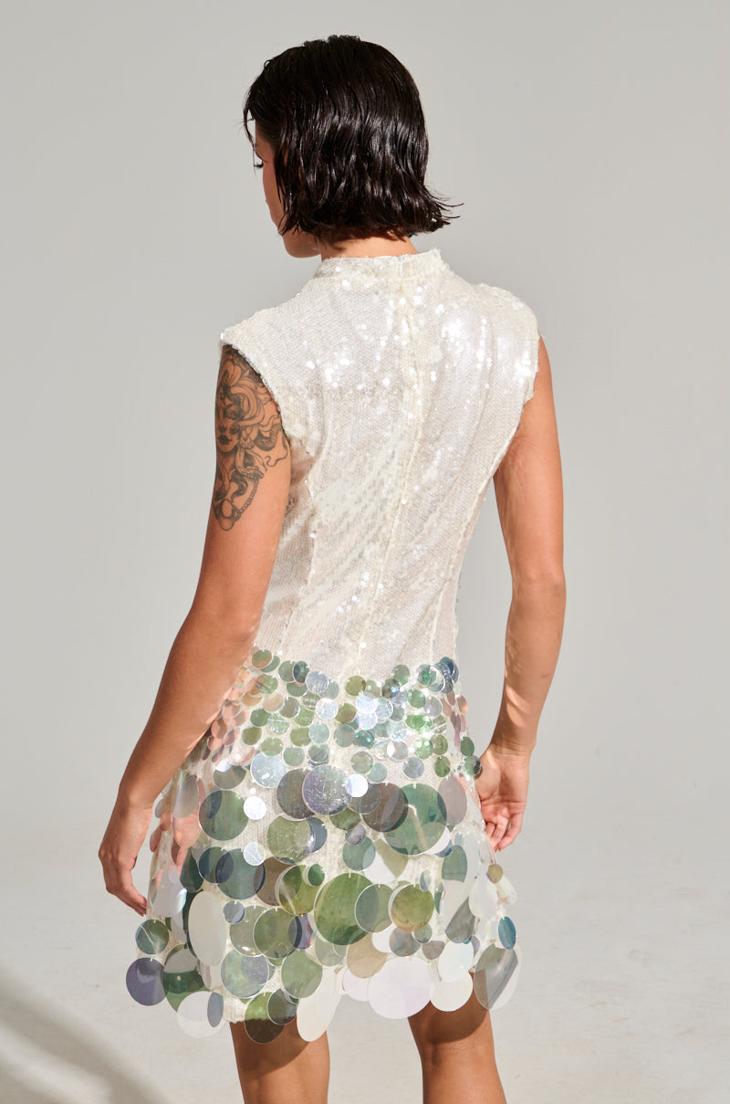 A person with wet hair and a tattoo on their left arm wears the ALL THE RIGHT WAYS SEQUIN MINI DRESS, a sleeveless, glittering outfit adorned with large, reflective sequins. This eye-catching party dress features a bodycon silhouette as they stand facing away against a plain background.