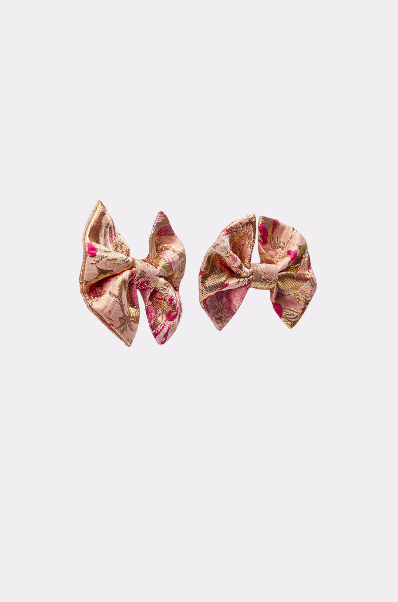 The REALLY ME BOW EARRINGS feature two pink and gold floral-patterned bows with intricate brocade-inspired designs, displayed side by side on a plain light background. 3