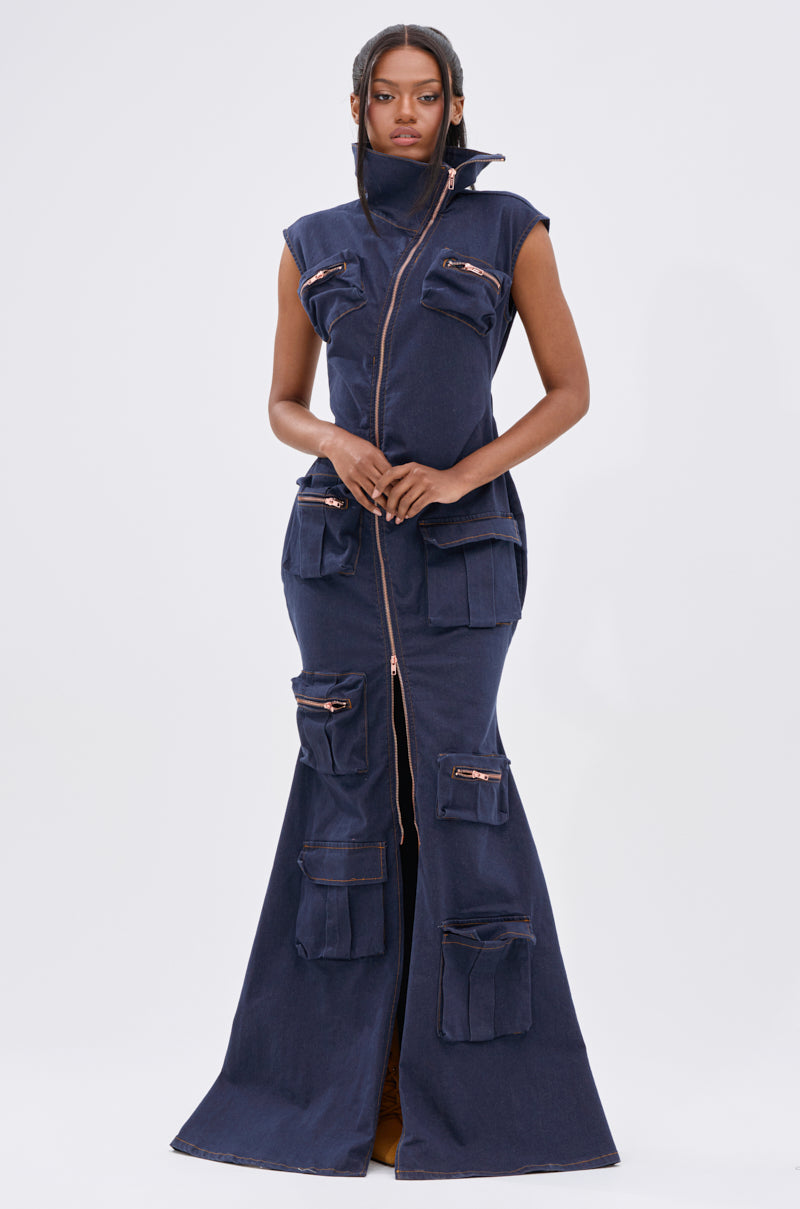 A woman faces forward in the DONT MESS WITH ME COLLARED DENIM MAXI DRESS, a dark wash, sleeveless maxi with a high collar, front zipper from neck to hem, and utility pockets with zippers and flaps for a modern, functional style.