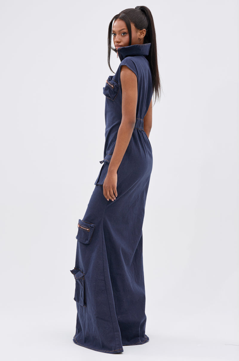 A woman with long straight hair in a high ponytail wears the DONT MESS WITH ME COLLARED DENIM MAXI DRESS, a sleeveless navy blue piece with utility pockets, standing sideways and looking at the camera.