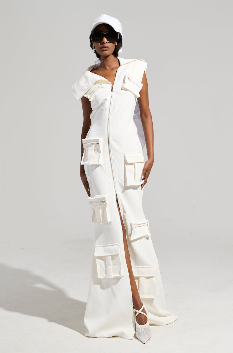 Wearing the DON'T MESS WITH ME COLLARED MAXI DRESS, a person stands confidently, highlighting its utility pockets and front zipper. They accessorize with sunglasses, a white cap, and white pointed shoes against a simple light gray background.