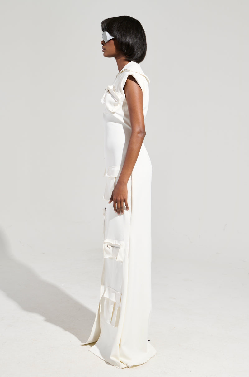 A woman stands in profile wearing the breathtaking DON'T MESS WITH ME COLLARED MAXI DRESS from the AKIRA Label, featuring large decorative bows. Her sleek black bob and white futuristic sunglasses perfectly complement the sophisticated ensemble, while the plain white background accentuates the dress's intricate design and modern style.