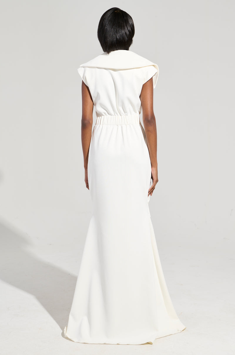 A person stands facing away, wearing the DON'T MESS WITH ME COLLARED MAXI DRESS, featuring a gathered waistline and structured shoulders. The elegant white fabric flows to the floor, creating a sleek silhouette against a plain background.