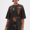 A person with wet-look slicked-back hair wears the MARGOT DISTRESSED STUDDED SHORT SLEEVE TEE, featuring large slashes, safety pins, and chains over a striped top, accessorized with hoop earrings and a cross necklace.