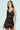 The woman in the "SHOW US WHAT YOU GOT SATIN MINI DRESS," a chocolate satin mini dress with lace trim, stands against a light green background. Her long brown hair enhances the bodycon fit, and she gazes at the camera with a neutral expression.