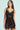 Against a light turquoise backdrop, a person with long hair wears the "SHOW US WHAT YOU GOT SATIN MINI DRESS" in sleek dark chocolate with lace trim, complemented by hoop earrings.