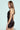 A woman with long brown hair stands in a three-quarter side pose against a light blue background, wearing the SHOW US WHAT YOU GOT SATIN MINI DRESS, which hugs her figure. She looks over her shoulder, smiling slightly.