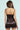 A woman with long brown hair faces away from the camera, wearing the SHOW US WHAT YOU GOT SATIN MINI DRESS. This chocolate satin dress features elegant black lace trim and a bodycon fit that highlights her silhouette against a light turquoise background.