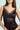A woman in a black SHOW US WHAT YOU GOT SATIN MINI DRESS with lace trim stands against a light blue background. Long, straight hair and large hoop earrings complement the dress's bodycon fit, while her hands rest by her sides, accentuating its lace detailing on the neckline and sides.