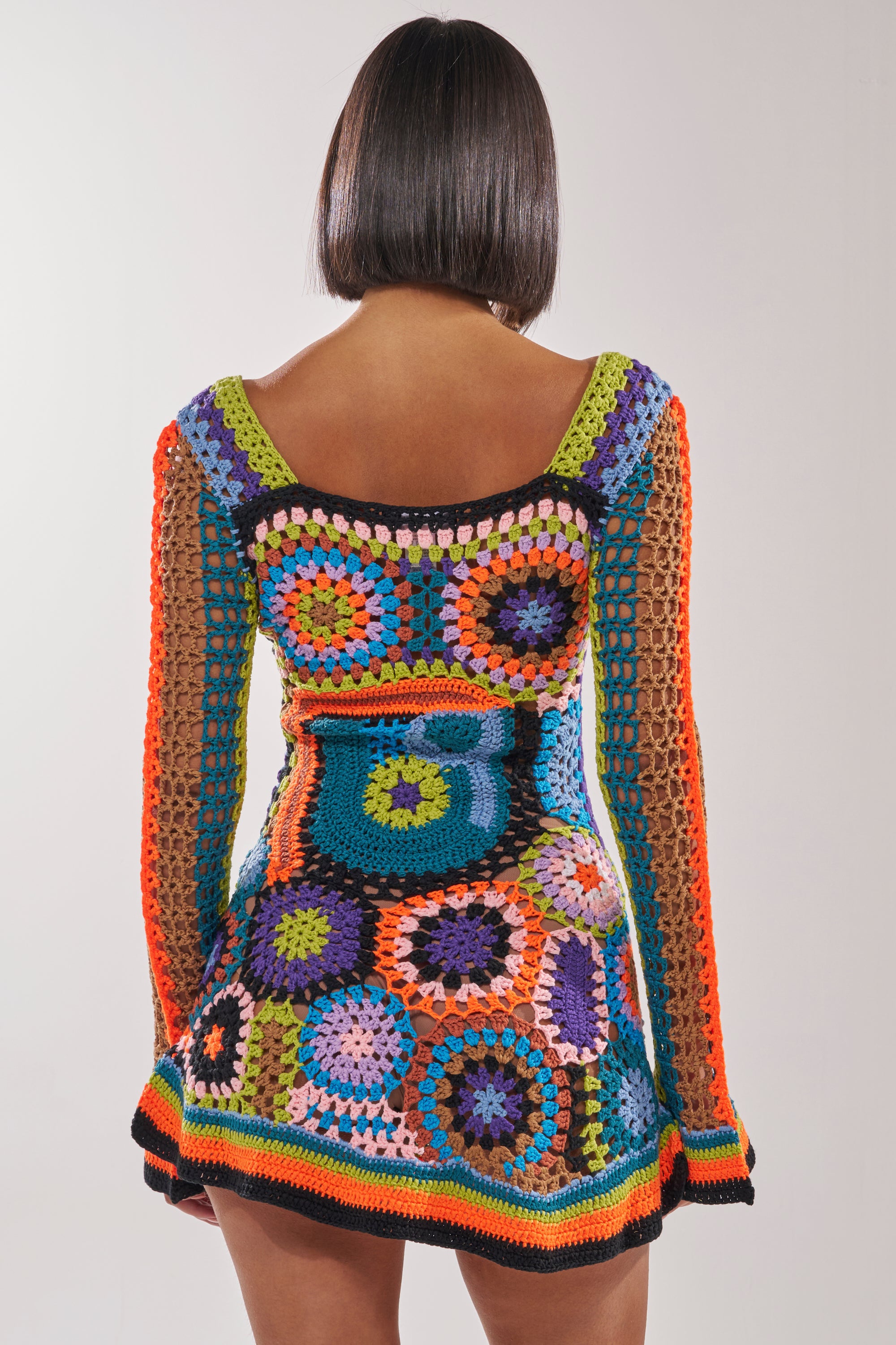 A person with a short bob is seen from behind in a PARADISE FOUND KNIT MINI DRESS, featuring vibrant geometric and circular boho-chic patterns. The background is plain and light. 3