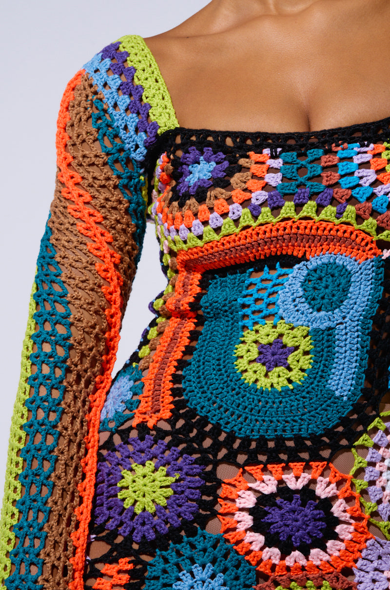 Close-up of a boho-chic dress being worn by a person. This PARADISE FOUND KNIT MINI DRESS features intricate crochet fabrication with vibrant colors and patterns, including green, blue, orange, purple, and black, showcasing a beautiful mix of floral and geometric designs.