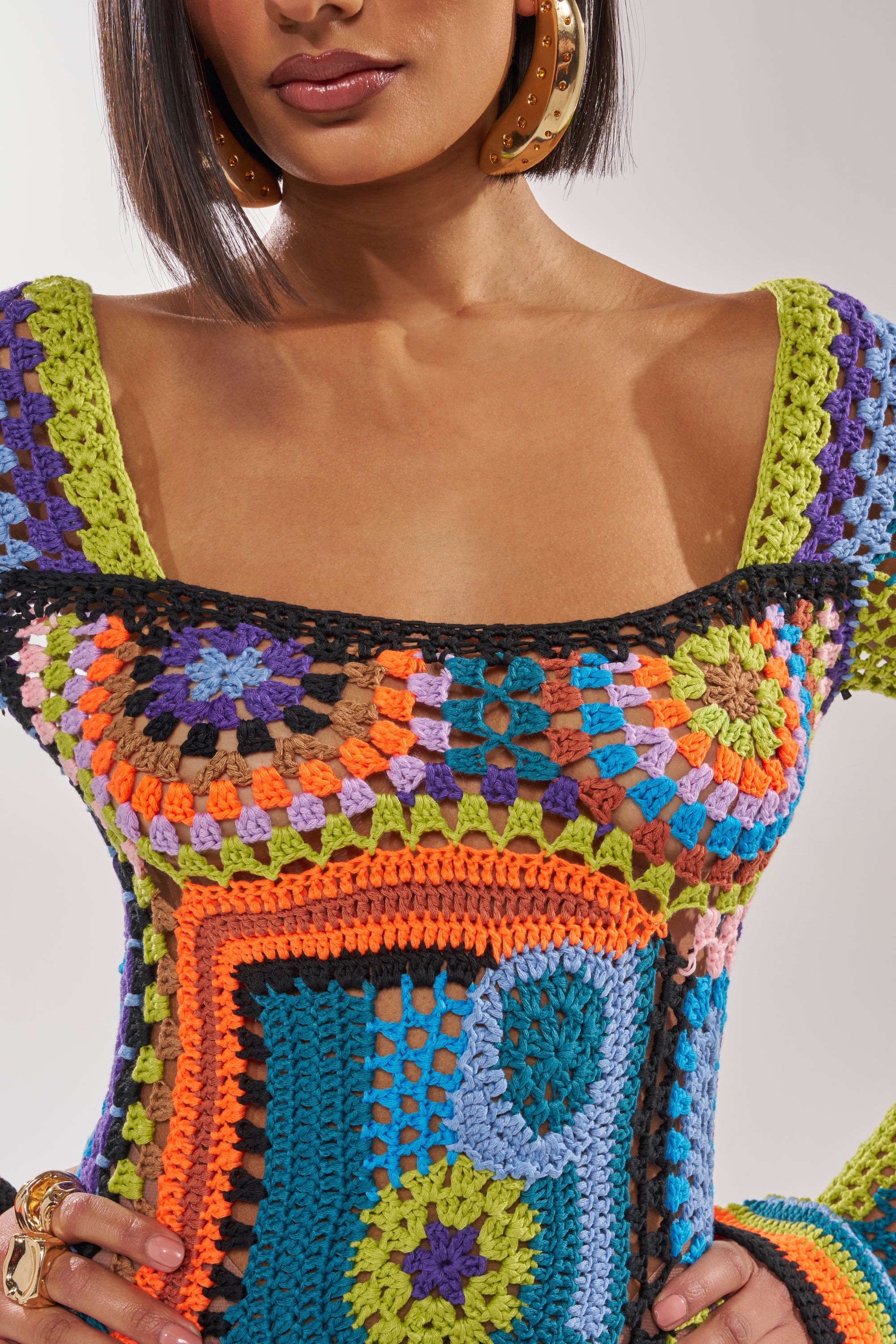 A woman wearing large gold hoop earrings and the PARADISE FOUND KNIT MINI DRESS, a colorful crochet mini dress with geometric patterns in vibrant green, blue, orange, pink, and black. 7