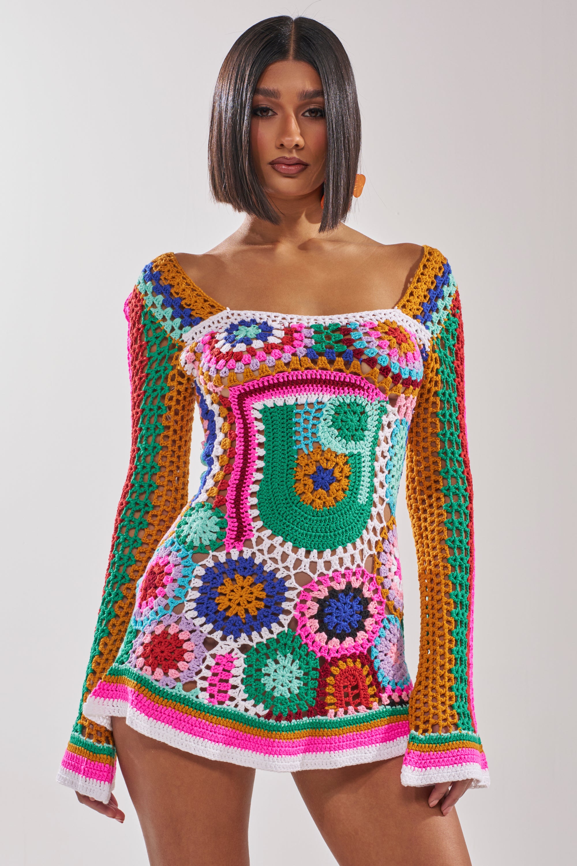 A woman with a sleek bob wears the CROCHET ALL DAY COLORBLOCK MINI DRESS, a vibrant crochet mini dress with bold geometric and floral patterns, posing against a plain light background. 0