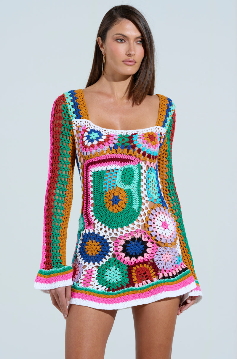 A woman models the Crochet All Day Colorblock Mini Dress, showcasing its colorful geometric patterns in vibrant green, pink, blue, orange, and white with bell sleeves. The vibrant dress pops against a neutral backdrop.