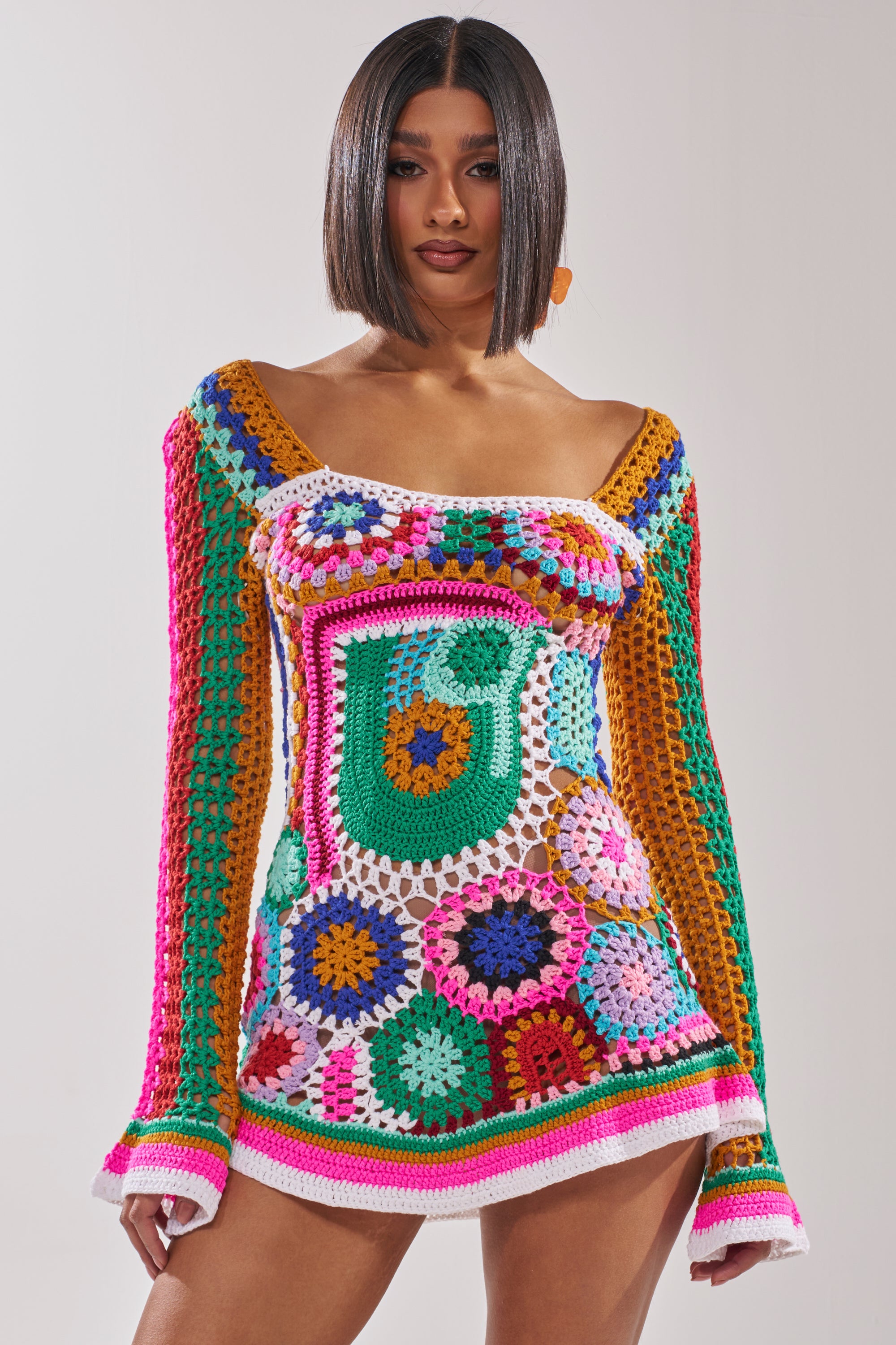 A woman with a sleek bob wears the CROCHET ALL DAY COLORBLOCK MINI DRESS, a colorful crochet mini with bell sleeves, showcasing geometric patterns in vibrant pink, green, yellow, blue, and white. 2