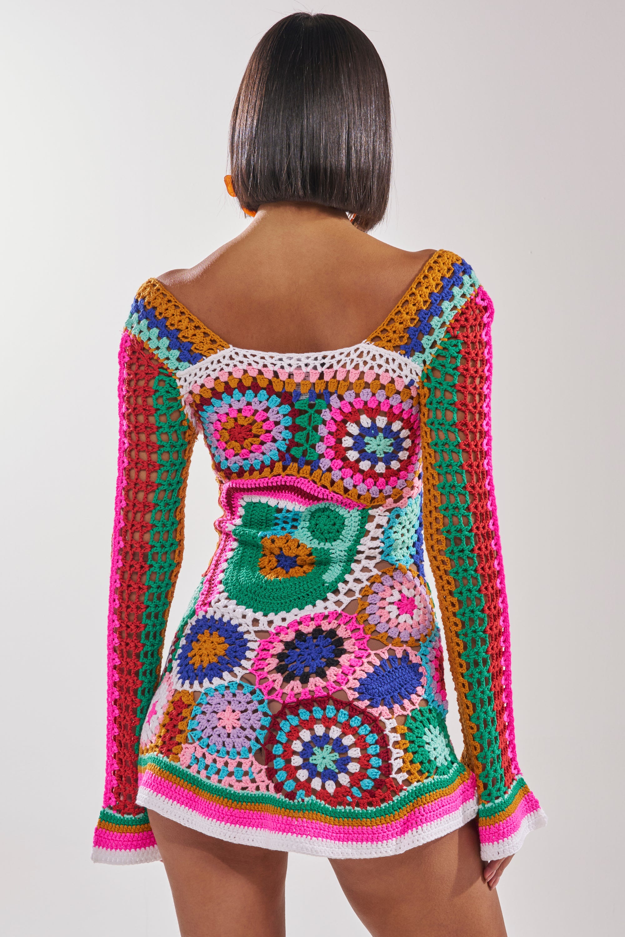 A person with straight, dark hair stands facing away against a plain white background, wearing the CROCHET ALL DAY COLORBLOCK MINI DRESS featuring vibrant patterns and circular motifs. 4
