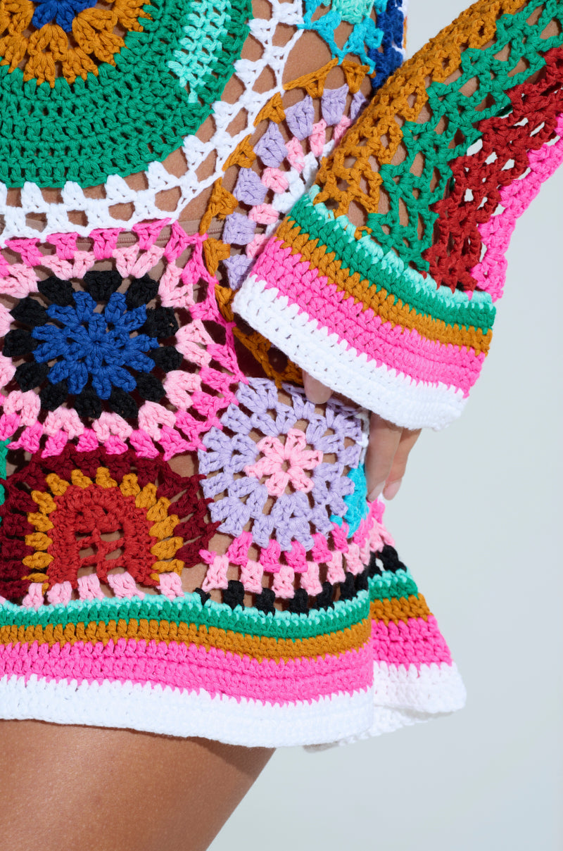 The CROCHET ALL DAY COLORBLOCK MINI DRESS features vibrant hues of pink, green, red, blue, and yellow in intricate crochet patterns. This eye-catching dress covers the arm and midsection with stylish bell sleeves for an elegant touch.