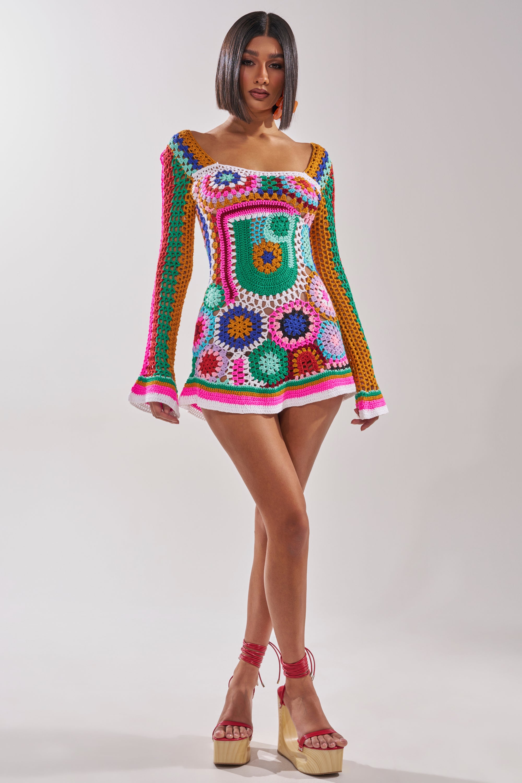 Wearing the CROCHET ALL DAY COLORBLOCK MINI DRESS, a woman stands confidently in platform sandals with ankle straps. The dress features vibrant patterns and bright hues, set against a plain light background. 7