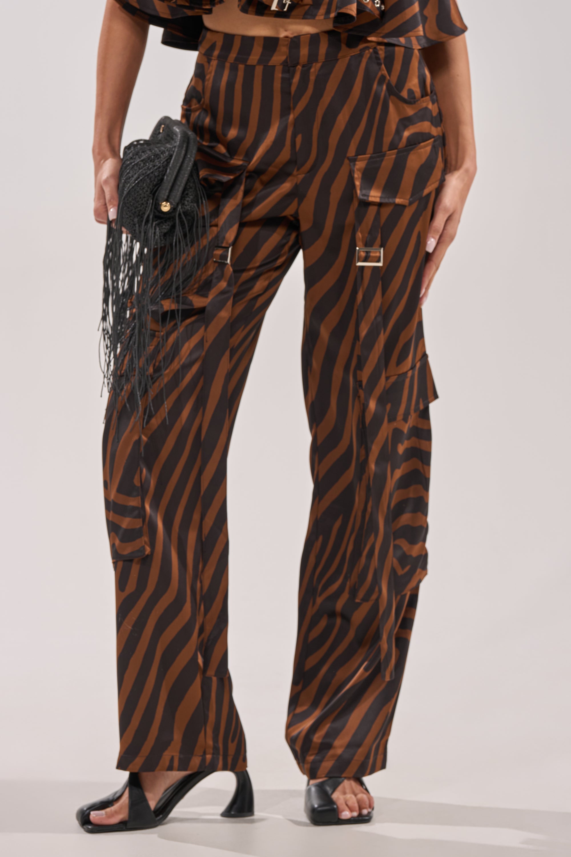 Wearing the INTO THE WILD ZEBRA TROUSER with cargo pockets, styled with a black fringed clutch and black open-toe heels. 2