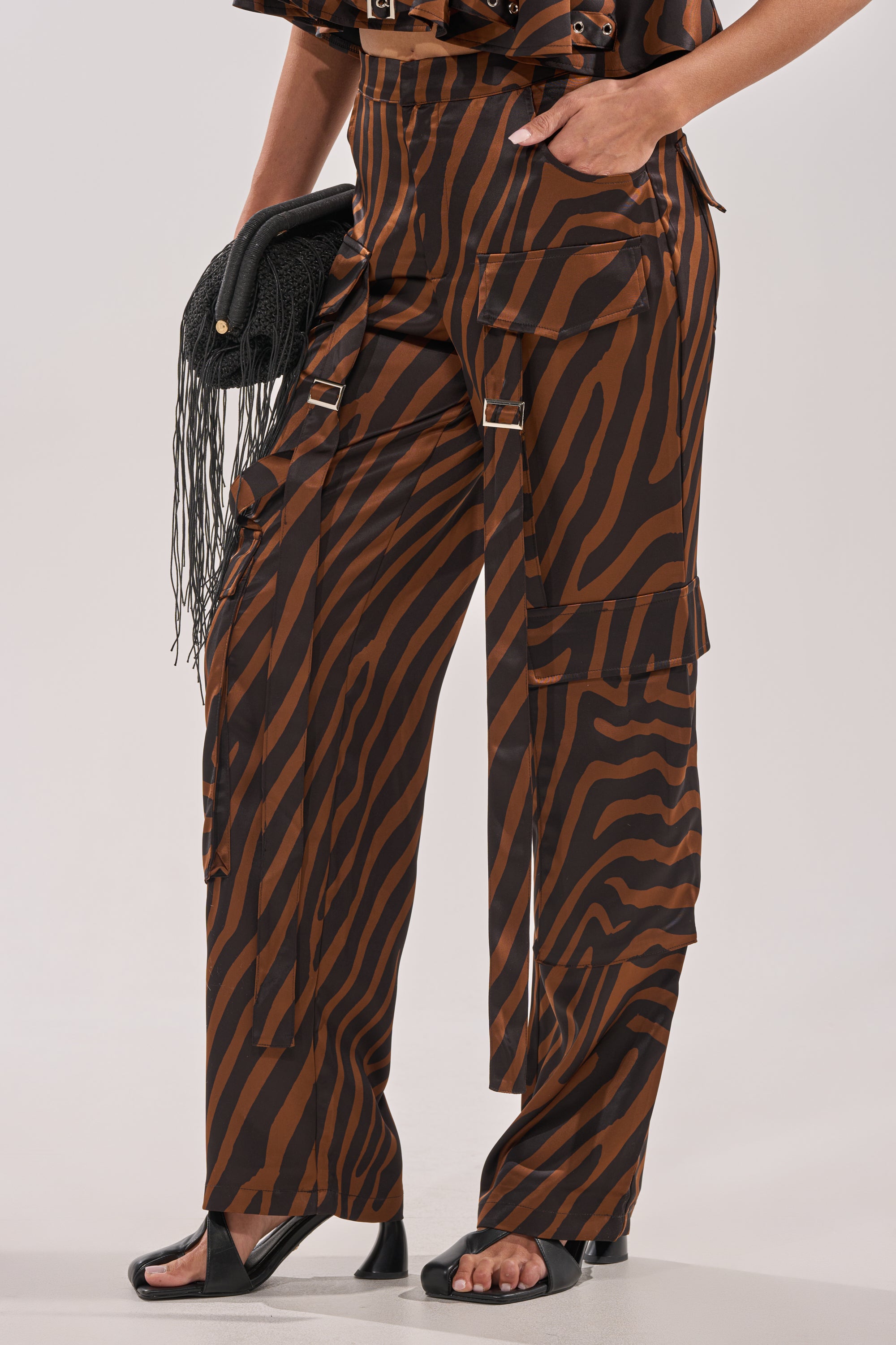 Wearing the INTO THE WILD ZEBRA TROUSER with multiple straps and buckles, paired with black open-toe heels and a black fringed clutch. 4