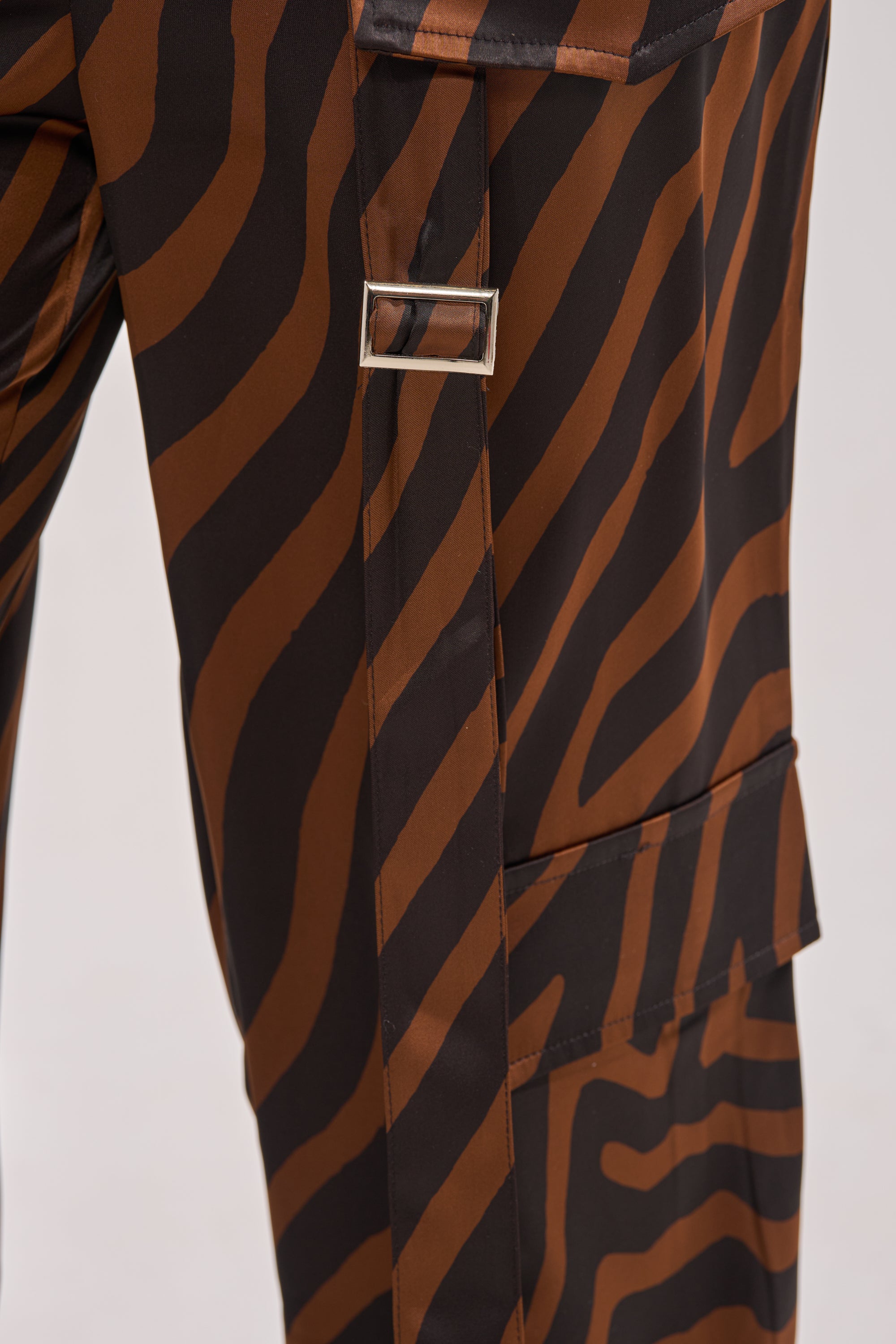 Close-up of the INTO THE WILD ZEBRA TROUSER, featuring a brown and black zebra print with a silver rectangular buckle and side flap pocket, crafted in a high-rise utility silhouette. 8