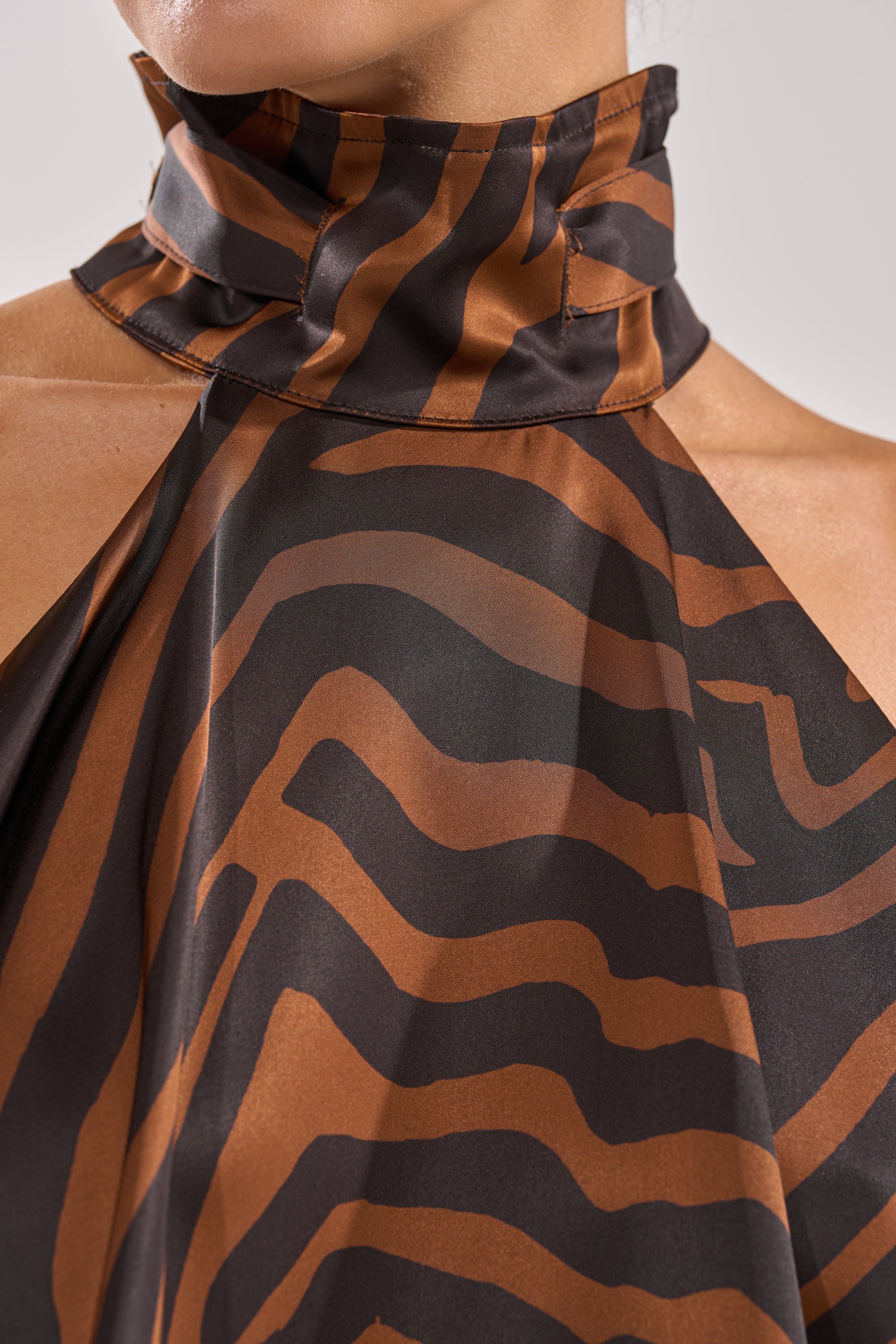 Close-up of a person wearing the INTO THE WILD ZEBRA HALTER NECK BLOUSE, featuring a brown and black zebra print, high-neck halter top, ruffled collar, and bold abstract pattern on smooth satin fabric for a modern edge. 9