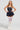 A person in a blue pinstripe Felt Cute Poplin mini dress, accessorized with layered pearl necklaces, white lace stockings, and high white boots, stands confidently against a plain backdrop.