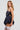 A woman with long blonde hair poses confidently in the FELT CUTE POPLIN Mini Dress in a stylish dark blue pinstripe, featuring a voluminous skirt and strapless neckline. She accessorizes with layered pearl necklaces and white lace thigh-high stockings against a plain backdrop.