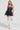 A woman stands confidently in the Felt Cute Poplin Mini Dress in Blue Pinstripe, featuring a strapless neckline. She accessorizes with layered pearl necklaces, white lace thigh-high stockings, and knee-high white lace-up boots. Her long, wavy hair flows down over her shoulders.