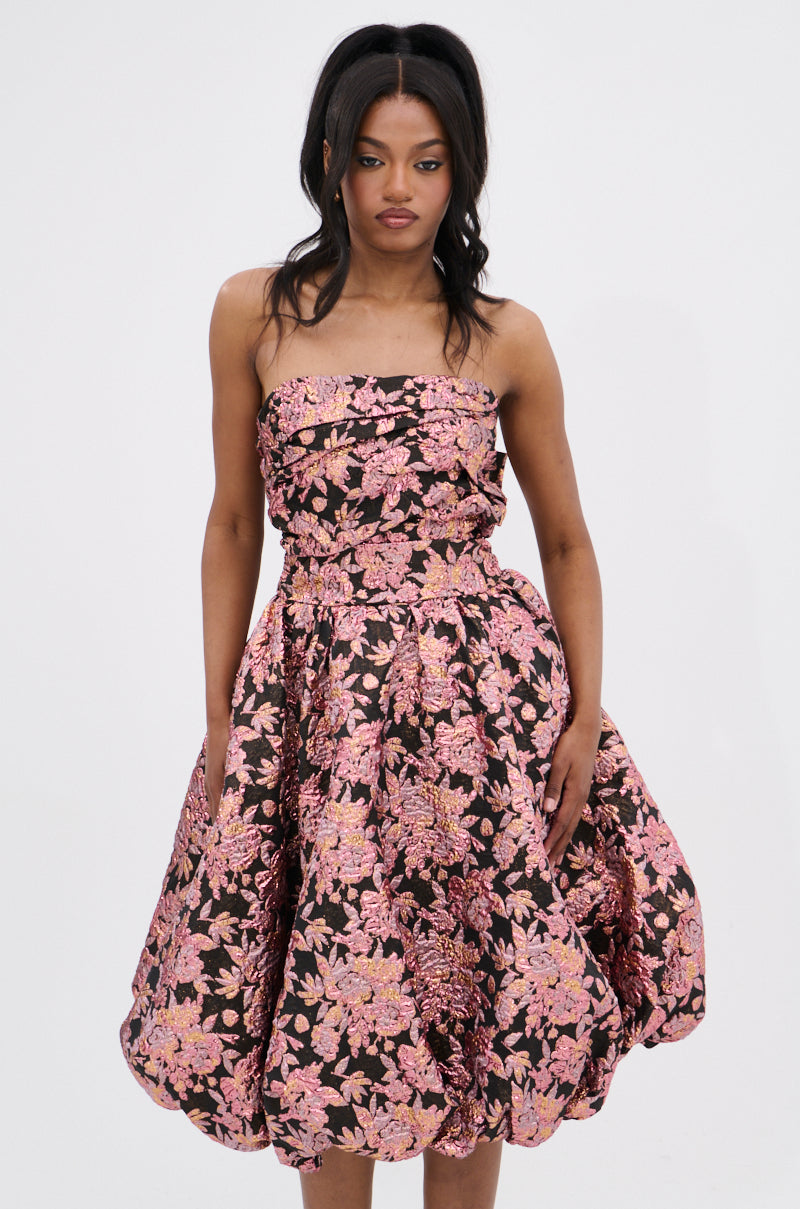 A woman with long, wavy dark hair poses against a white background in the CHARLOTTE BROCADE MIDI DRESS, which showcases a strapless ruched bodice, full skirt, and metallic pink floral brocade print.