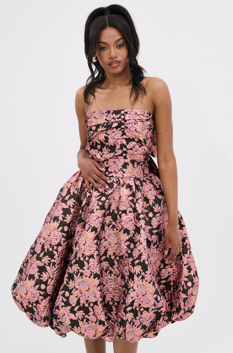 A woman models the CHARLOTTE BROCADE MIDI DRESS, showcasing its ruched bodice and voluminous skirt with a pink metallic brocade print on black, posed against a plain white background.