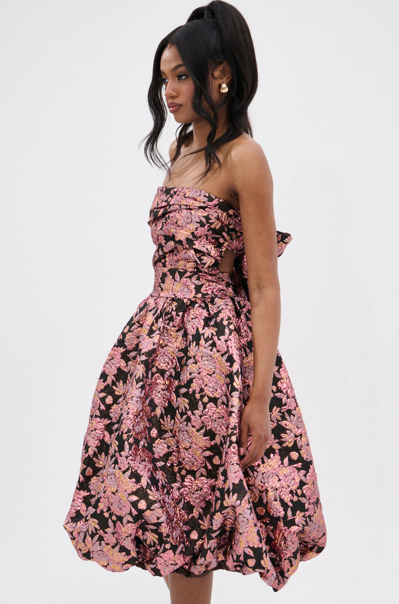 Woman in the CHARLOTTE BROCADE MIDI DRESS—strapless, knee-length with a voluminous skirt. The metallic pink and gold floral brocade dress has a ruched bodice. Her long dark hair is styled in a high ponytail against a white background.