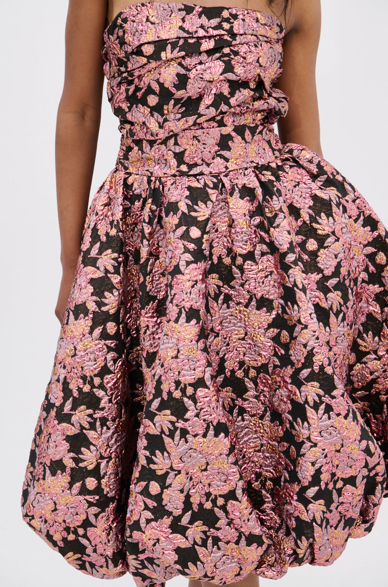Someone is wearing the CHARLOTTE BROCADE MIDI DRESS, a strapless midi with a ruched bodice and full skirt in black, detailed with pink and gold metallic brocade. The image is cropped to show just the torso and upper legs.
