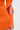 A close-up of a person wearing the OFF TO BRUNCH KNIT MINI DRESS IN ORANGE, featuring long sleeves, a stretchy ribbed fabric, and a unique open slit at the sleeve secured by four orange buttons near the wrist.