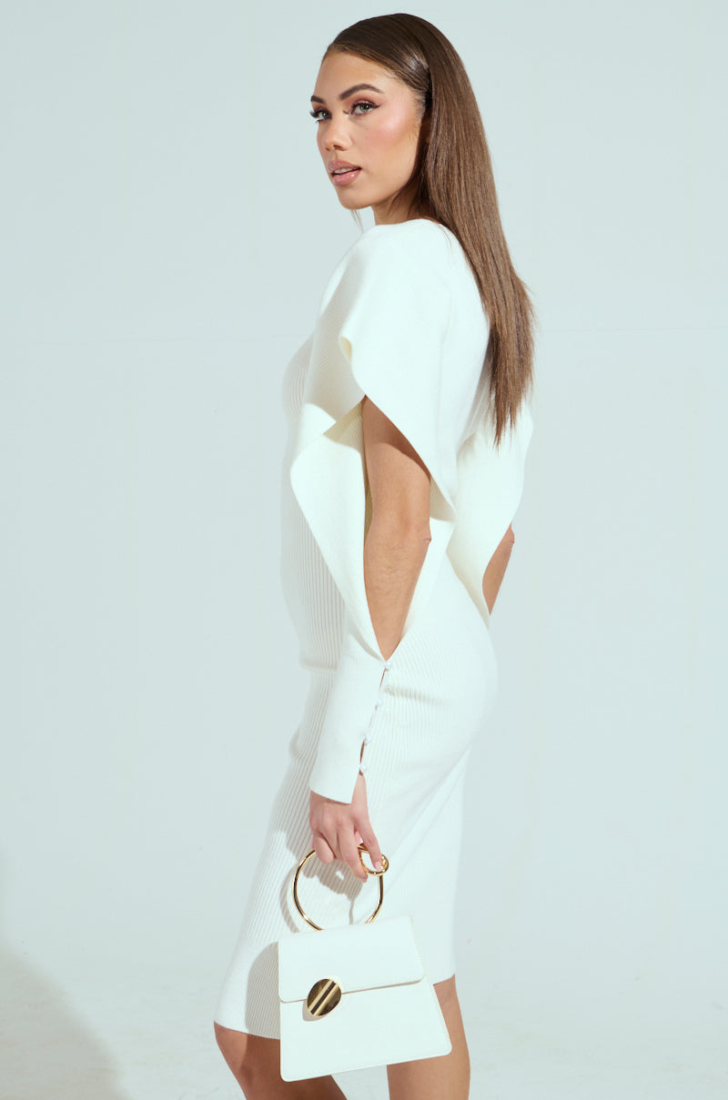 A woman with long brown hair wears the OFF TO BRUNCH KNIT MIDI DRESS in white, featuring a plunging neckline and short sleeves. She holds a white handbag with a circular handle and gold accent, standing against a plain light background, looking to the side.