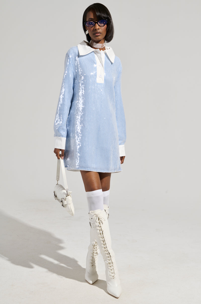 A chic AF individual is striking a pose in the CHIC AF Sequin Poplin Mini Dress in light blue, featuring a white collar. They complement their look with knee-high white lace-up boots, sunglasses, and a small white handbag while standing confidently against a plain background.